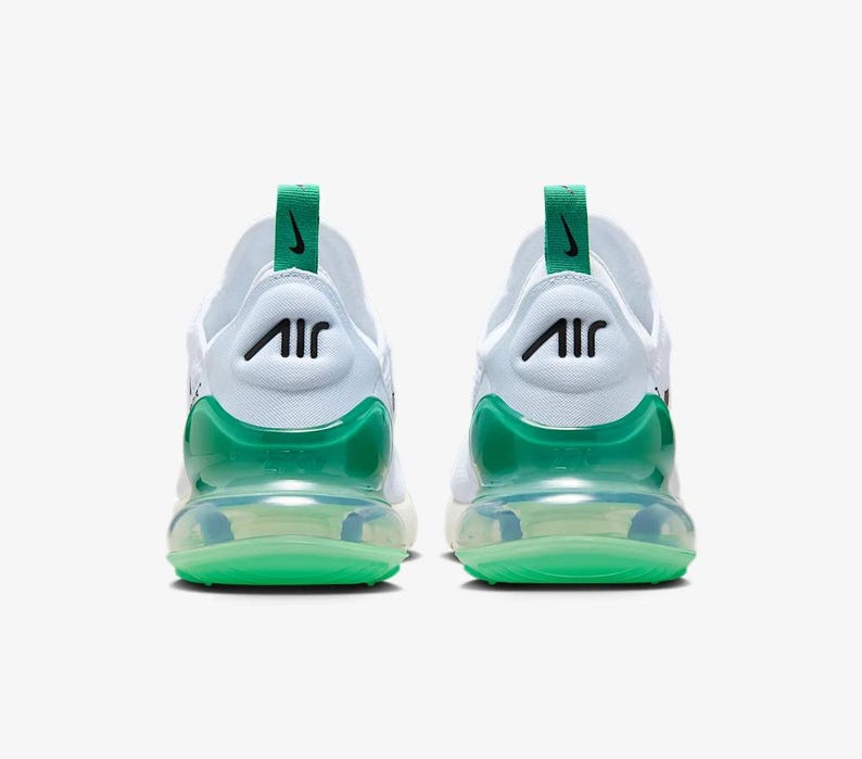 May include: Pair of white athletic shoes with green accents. The shoes feature a green heel counter and a green air bubble sole. The Nike Air logo is visible on the back of the shoe. The shoes are designed for athletic activities.