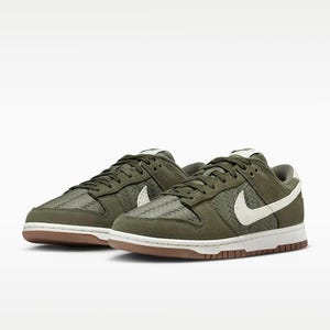 Puede incluir: Un par de zapatillas Nike Dunk Low verde oliva. Las zapatillas presentan una textura tejida en las superposiciones, logotipos de swoosh blancos y una suela exterior marr&oacute;n. Los cordones y la leng&uuml;eta son de color verde oliva y la entresuela es blanca.