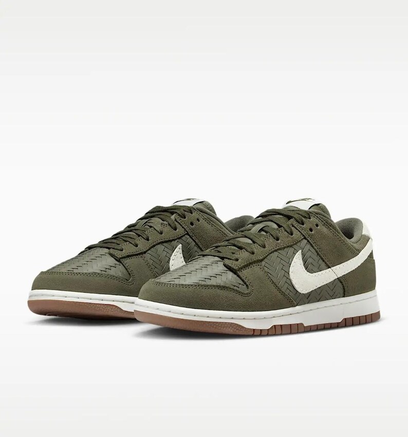 Puede incluir: Un par de zapatillas Nike Dunk Low verde oliva. Las zapatillas presentan una textura tejida en las superposiciones, logotipos de swoosh blancos y una suela exterior marr&oacute;n. Los cordones y la leng&uuml;eta son de color verde oliva y la entresuela es blanca.