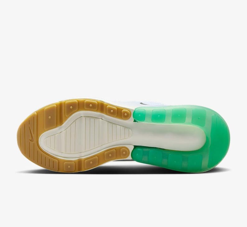May include: Bottom view of a white and green athletic shoe. The sole features a brown rubber heel and toe, with a white and green midsole. The shoe's design includes a visible air unit in the heel, and a textured pattern on the sole.