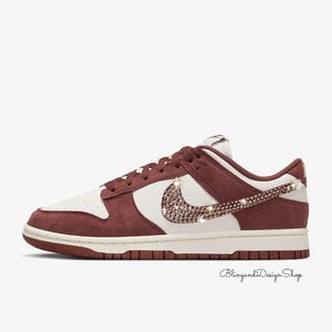 Può includere: Una sneaker bassa bianca, bordeaux e marrone. Lo swoosh Nike è impreziosito da strass. I lacci e le finiture sono bordeaux. La suola è marrone. Il testo "BlingandDesign Shop" è in basso.