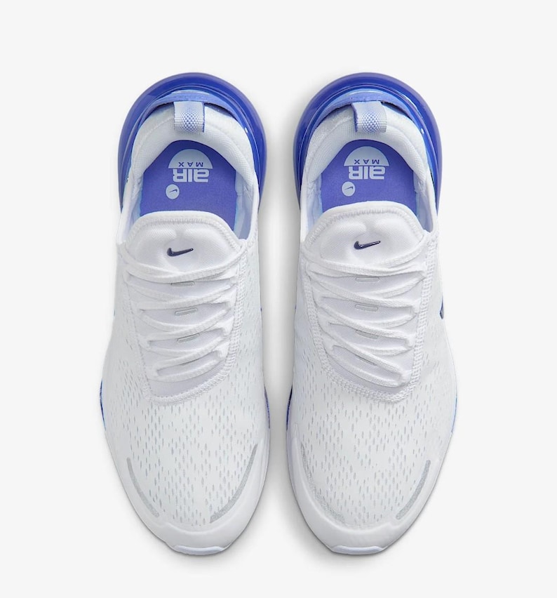 Op de afbeelding: Bovenaanzicht van witte sportschoenen met blauwe accenten. De schoenen hebben een mesh bovenwerk, witte veters en een blauwe hielkap. Het Nike-logo is zichtbaar. De zool is wit met een blauwe luchtbel.