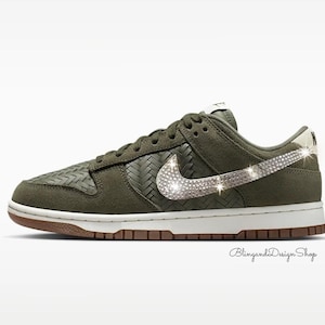 Puede incluir: Zapatillas Nike Dunk Low verde oliva con entresuela blanca y suela marr&oacute;n. El logo de Nike est&aacute; adornado con brillantes pedrer&iacute;a. El zapato presenta una textura tejida en los laterales y la puntera.