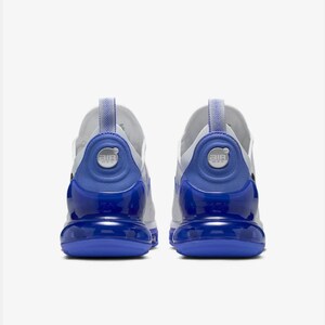 Op de afbeelding: Paar witte en blauwe sportschoenen. De schoenen hebben een wit bovenwerk met blauwe accenten op de hiel en zool. De hiel heeft een cirkelvormig ontwerp met het woord "AIR" erop gedrukt. De zolen zijn felblauw.