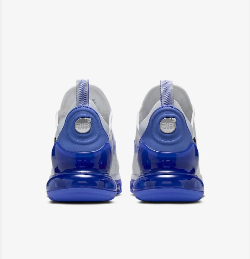 Op de afbeelding: Paar witte en blauwe sportschoenen. De schoenen hebben een wit bovenwerk met blauwe accenten op de hiel en zool. De hiel heeft een cirkelvormig ontwerp met het woord "AIR" erop gedrukt. De zolen zijn felblauw.