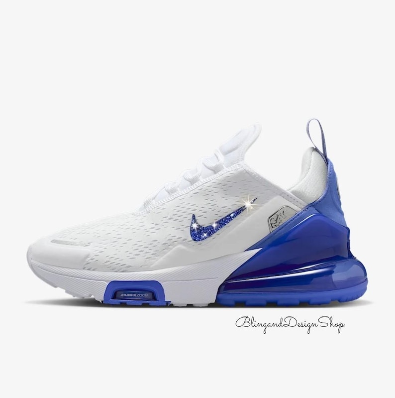 Op de afbeelding: Witte en blauwe sportschoen met een sprankelende blauwe Nike swoosh. De schoen heeft een wit mesh bovenwerk, een blauwe hielkap en een blauwe zool. De tekst "AIR 270" is zichtbaar op de zijkant van de schoen. De tekst "BlingandDesign Shop" is cursief geschreven.