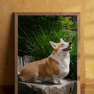 May include: A framed print of a Corgi dog, with a brown and white coat, sitting on a stone. The background features green foliage and a wooden fence. The artwork is set against a yellow wall.