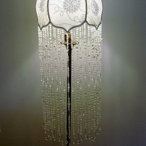 May include: A white floor lamp with a beaded fringe and a floral patterned lampshade.