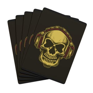 Puede incluir: Un juego de cartas con fondo negro. Cada carta presenta una calavera dorada con auriculares rojos y dorados. La calavera tiene sombreado detallado y una expresión severa. Las cartas están abanicadas, mostrando el diseño.
