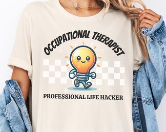 Op de afbeelding: Crèmekleurig T-shirt met de tekst "OCCUPATIONAL THERAPIST" boven een cartoon gloeilamp karakter en de tekst "PROFESSIONAL LIFE HACKER" eronder. De gloeilamp is oranje en geel met blauwe benen en armen. De achtergrond heeft een dambordpatroon.