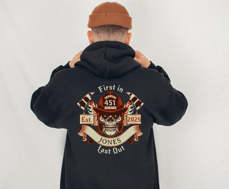 Puede incluir: Sudadera negra con un gr&aacute;fico de un casco de bombero con una calavera y huesos cruzados. El gr&aacute;fico incluye el texto "First in Last Out", "Chicago Firefighter", "Est. 2025", y "Jones".