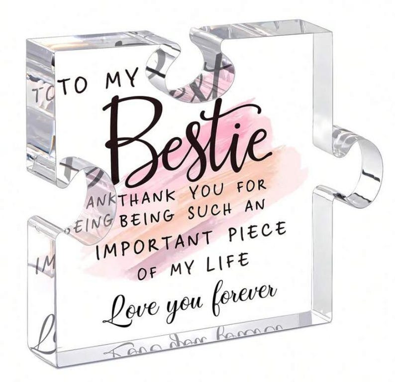 Op de afbeelding: Transparant acryl puzzelstuk met de woorden "TO MY Bestie" in zwart script. De tekst "THANK YOU FOR BEING SUCH AN IMPORTANT PIECE OF MY LIFE Love you forever" staat ook op het puzzelstuk. Een roze en perzik aquarelontwerp staat achter het woord "Bestie".