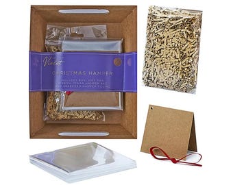 Op de afbeelding: Een bruine kartonnen kerstcadeaudoos met een paarse band met de tekst "CHRISTMAS HAMPER". Inclusief cadeaukaart, lint, doorzichtige cadeauzak en versnipperde vulling. Een doorzichtige zak met versnipperd papier en een gevouwen cadeaukaart met een rood lint zijn ook inbegrepen.