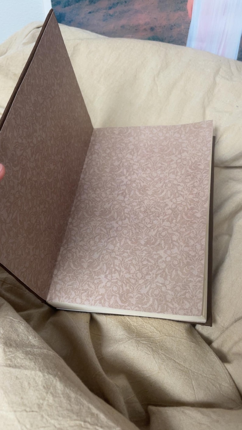 Puede incluir: Diario abierto con una cubierta marr&oacute;n y p&aacute;ginas con estampado floral. Las p&aacute;ginas son de color beige claro con un dise&ntilde;o floral delicado y repetitivo. El diario est&aacute; abierto, revelando las p&aacute;ginas interiores.