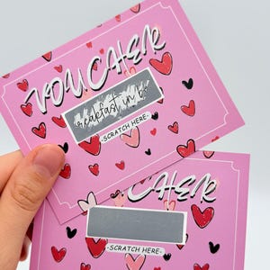 May include: Two pink scratch-off cards with a heart pattern. The top card says "You Can" with a silver scratch-off area that says "Breakfast in Bed". The bottom card says "Cher" with a silver scratch-off area.