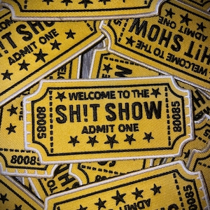 May include: Yellow embroidered patches with the text "WELCOME TO THE SH!T SHOW" and "ADMIT ONE". The patches have a ticket design with black text, stars, and the number "80085".