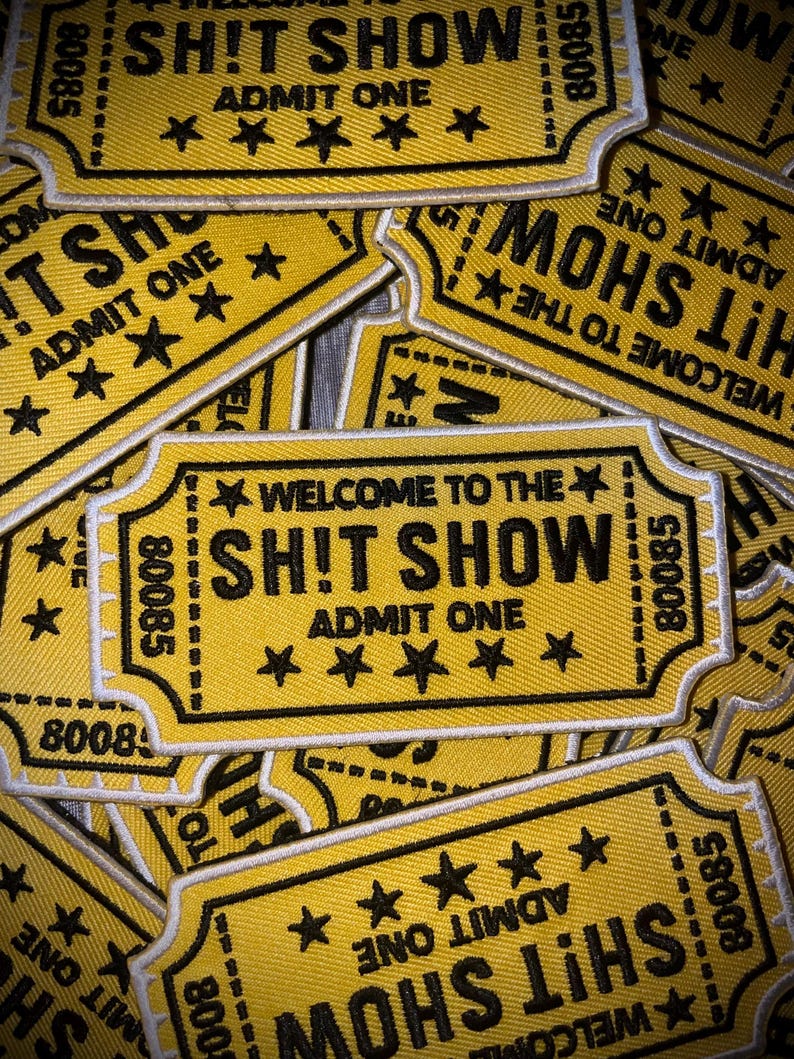 May include: Yellow embroidered patches with the text "WELCOME TO THE SH!T SHOW" and "ADMIT ONE". The patches have a ticket design with black text, stars, and the number "80085".