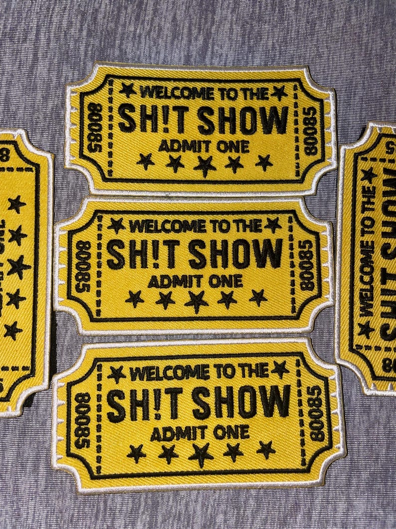May include: Yellow embroidered patches with black text that reads "WELCOME TO THE SH!T SHOW ADMIT ONE" and five black stars. The patches have a ticket shape with a white border and the number "80085".