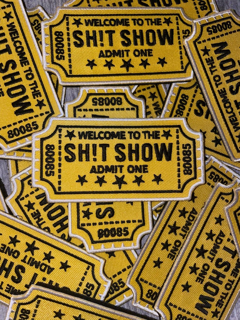 May include: A collection of yellow and black fabric patches. Each patch is shaped like a vintage ticket and features the text "WELCOME TO THE SH!T SHOW" and "ADMIT ONE". The patches have a star design and the number "80085".