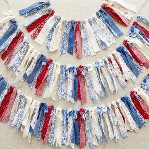 Puede incluir: Tres guirnaldas de tela patrióticas con cintas estampadas en rojo, blanco y azul. Las cintas están atadas a un cordel natural, creando una pancarta decorativa. Adecuadas para el Día de la Independencia u otras celebraciones patrióticas.