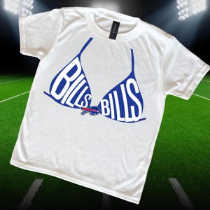 May include: White t-shirt featuring a blue bra design with the word "BILLS" in white letters. The Buffalo Bills logo is centered below the bra design. The shirt is made of a soft material.