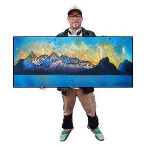 Könnte beinhalten: Gerahmtes Landschaftsgemälde mit einer Bergkette mit schneebedeckten Gipfeln. Das Kunstwerk zeigt einen blauen See und einen Himmel mit orange-gelben Farbtönen. Das Gemälde ist unten rechts signiert.