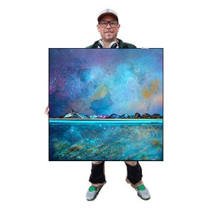 Puede incluir: Impresión artística abstracta cuadrada que representa un paisaje cósmico con una cordillera y agua. La obra de arte utiliza azules, morados y naranja, creando una atmósfera de ensueño. La impresión está enmarcada en un borde negro. Aproximadamente 60 cm x 60 cm.