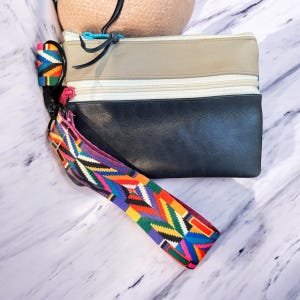 May include: A black and beige leather clutch with a zipper closure and a colorful patterned strap.