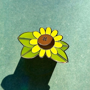 Könnte beinhalten: Eine gelbe Sonnenblume mit brauner Mitte und einem Hashtag-Symbol darin. Die Sonnenblume hat grüne Blätter.