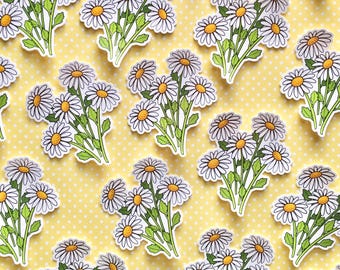 Op de afbeelding: Een vel met witte madeliefjes stickers op een gele achtergrond met witte stippen. De madeliefjes zijn wit met gele centers en groene stelen en bladeren.