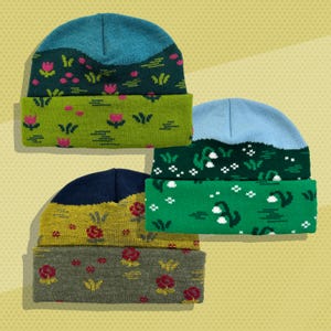 May include: Three knitted beanies with different floral patterns. The first beanie is blue and green with pink flowers. The second beanie is blue and green with white flowers. The third beanie is navy blue and yellow with red flowers.