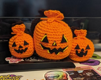 May include: Three crocheted orange pumpkins with black felt faces. The pumpkins are different sizes and are sitting on a table with stickers.