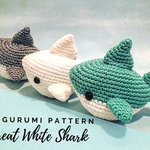 May include: Three crocheted amigurumi great white shark toys. The sharks are gray, white, and teal. The text "AMIGURUMI PATTERN Great White Shark" is at the bottom of the image.