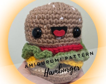 May include: A crocheted amigurumi hamburger toy with a smiling face, black eyes, and a red mouth. The hamburger is layered with green lettuce, yellow cheese, and red tomato.