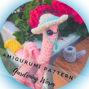 May include: A crocheted pink worm wearing a hat and sunglasses, with a small watering can. The worm has a yellow tail and is labeled "Amigurumi Pattern Gardening Worm."