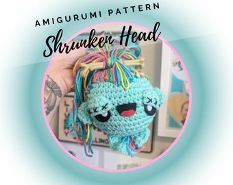 May include: An amigurumi crochet doll with a light blue head, black button eyes with stitched X marks, and a wide black mouth with a red tongue. The doll has multi-colored yarn hair tied with a tan bone-shaped accessory. Text reads AMIGURUMI PATTERN Shrunken Head.
