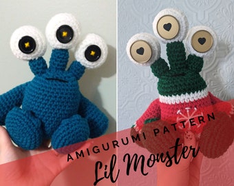 Peut inclure: Deux monstres amigurumi en crochet, l'un bleu avec trois yeux blancs et l'autre vert avec un pull rouge et blanc et trois yeux blancs avec des cœurs dorés. Le texte "AMIGURUMI PATTERN Lil monster" est en bas de l'image.