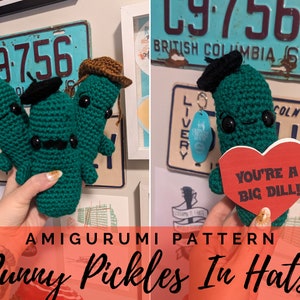 Pode incluir: Três brinquedos de amigurumi de picles verdes de crochê usando chapéus. O picles do meio usa um chapéu preto e um bigode. O picles à esquerda usa um chapéu preto e o picles à direita usa um chapéu marrom. O picles do meio está segurando um coração vermelho com o texto "You're a big dill!"