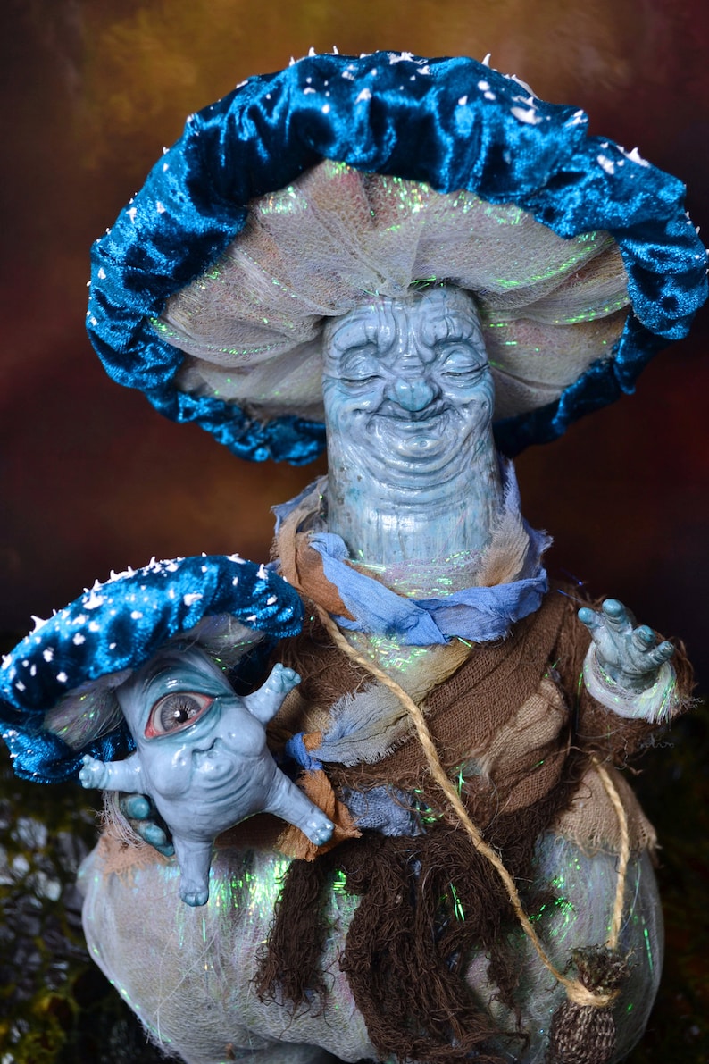Puede incluir: Una figura de champi&ntilde;&oacute;n azul y blanco con una figura de champi&ntilde;&oacute;n azul y blanco m&aacute;s peque&ntilde;a unida a su lado. La figura m&aacute;s grande tiene una cara sonriente y los ojos cerrados. La figura m&aacute;s peque&ntilde;a tiene un ojo grande y una cara sonriente.