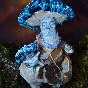 Puede incluir: Una figurita en forma de hongo azul y blanco con una cara sonriente y una figurita de hongo m&aacute;s peque&ntilde;a con un ojo en su mano.