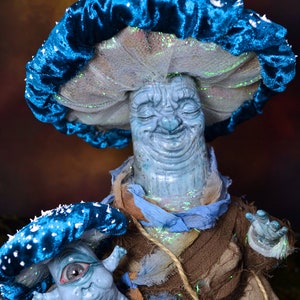 Puede incluir: Una figurita en forma de hongo azul y blanco con una cara sonriente, sosteniendo una figurita de hongo azul y blanco m&aacute;s peque&ntilde;a con un ojo grande.