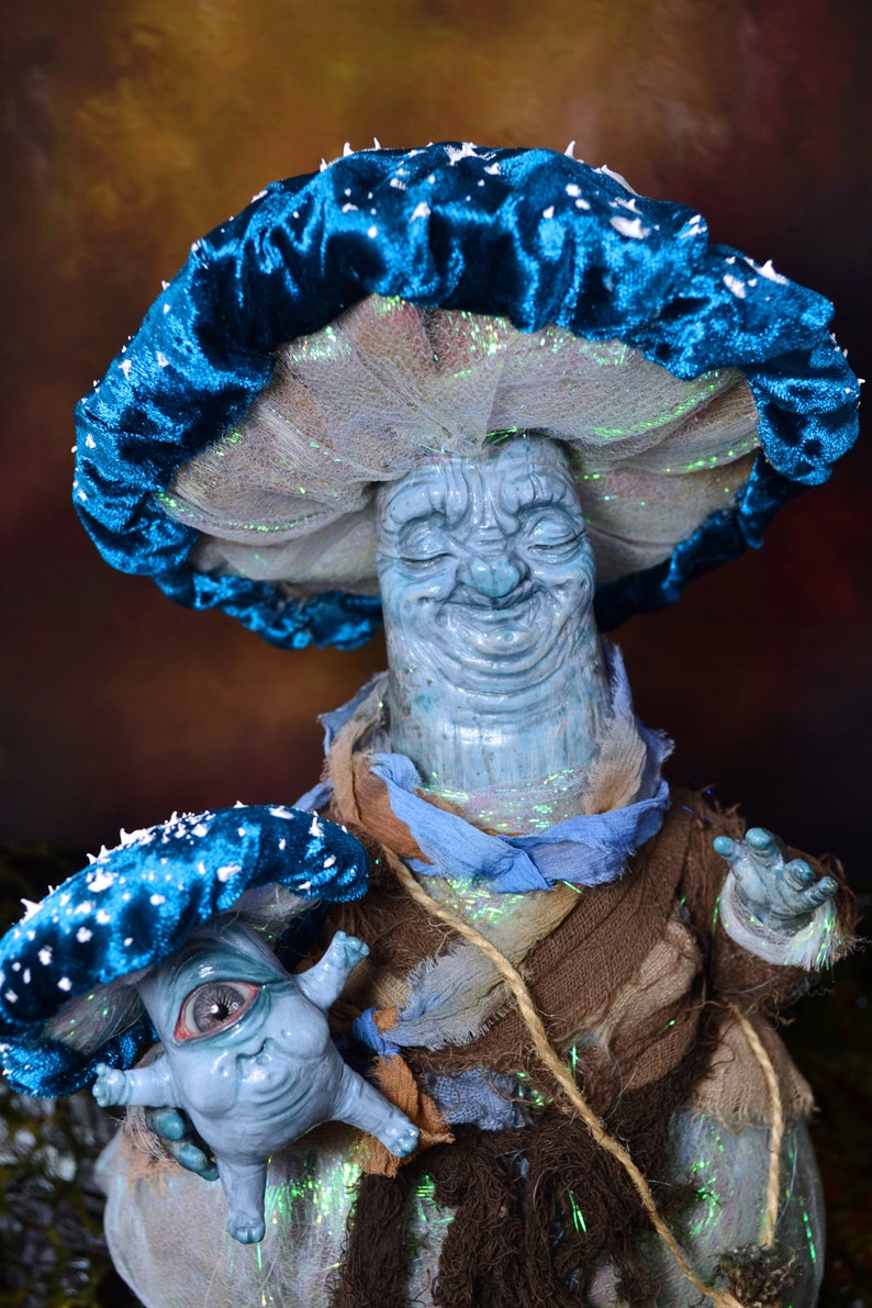 Puede incluir: Una figurita en forma de hongo azul y blanco con una cara sonriente, sosteniendo una figurita de hongo azul y blanco m&aacute;s peque&ntilde;a con un ojo grande.