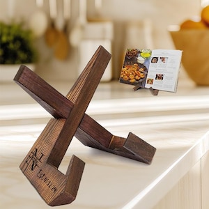 May include: A wooden cookbook stand with a rustic brown finish. The stand is in the shape of an X and has a personalized inscription that reads "The N Family Est. 01.22.21".