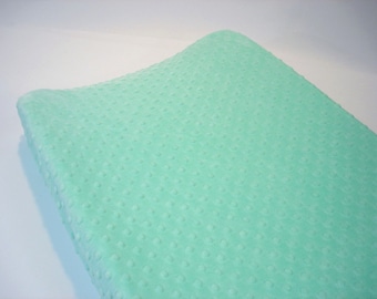 May include: A soft, light green changing pad cover with a textured, quilted surface.