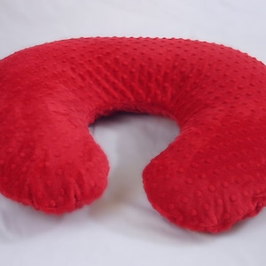 May include: A red, U-shaped nursing pillow with a textured, dotted surface. The pillow is designed to provide support for mothers during breastfeeding or for babies during tummy time.