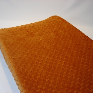 May include: A soft, orange changing pad cover with a textured, quilted pattern.
