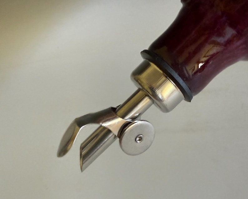 May include: A stainless steel bottle pourer with a hinged flap mechanism attached to a dark purple glass bottle neck. The metal spout features a circular side disc and a black rubber seal ring connecting the pourer to the bottle opening.
