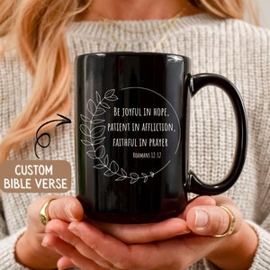 May include: Black ceramic mug with a white floral design and the text "BE JOYFUL IN HOPE, PATIENT IN AFFLICTION, FAITHFUL IN PRAYER" and "ROMANS 12:12".
