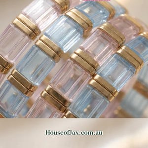 May include: A set of bracelets featuring alternating rectangular light pink and light blue glass beads separated by gold-toned metal spacers. Text on the image reads: Beaded beautiful bracelets, Your personal dopamine, You see your wrists every second, Mental health start with beautiful bracelets, HouseofJax.com.au, Your Daily Dose of Gold & Glass.
