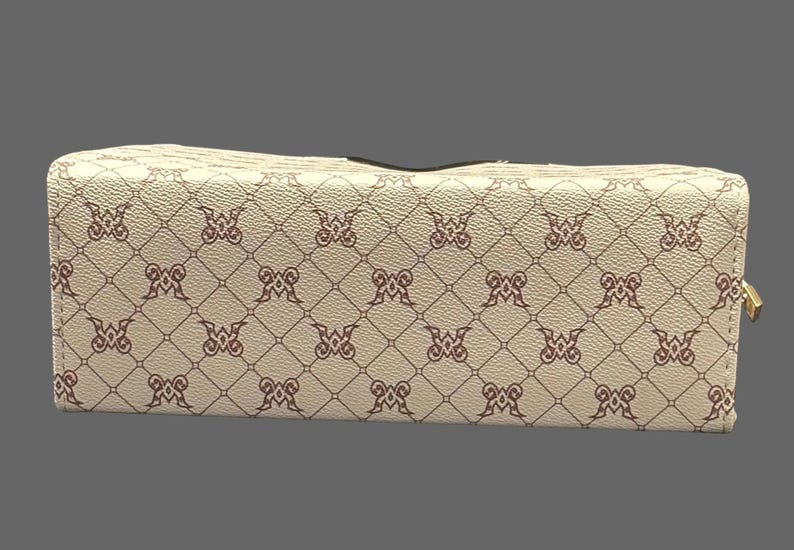 May include: A rectangular, cream-colored wallet with a repeating pattern of brown decorative elements. The wallet has a gold-colored zipper and a black interior. The pattern is a repeating design of the letter "M".